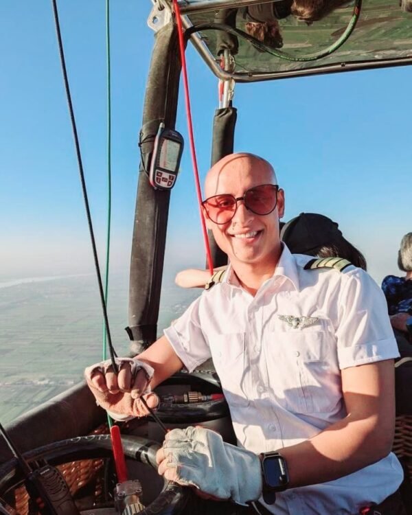 Captain Ali in the basket in pilot uniform, hands on the burner controls above Luxor