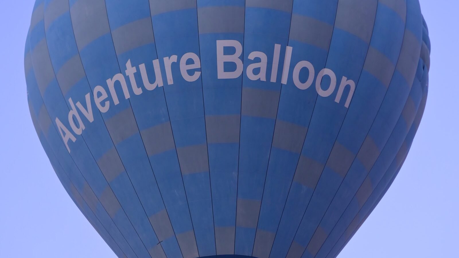 A deep blue hot air balloon marked Adventure Balloon climbing into a clear sky over Luxor