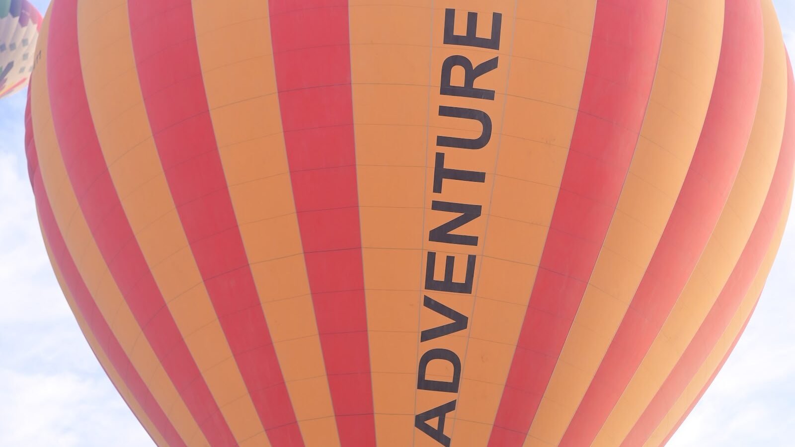 An orange and red hot air balloon with Adventure Balloon lettering flying over Luxor