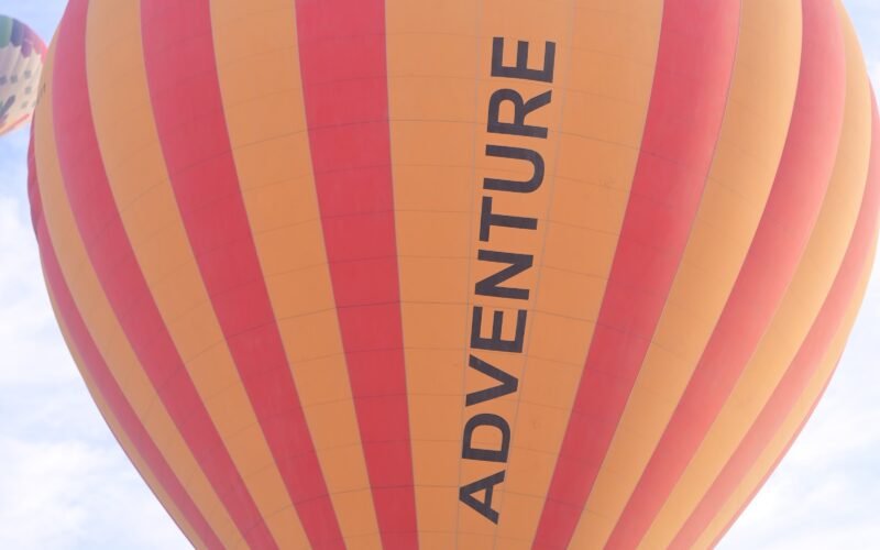 An orange and red hot air balloon with Adventure Balloon lettering flying over Luxor