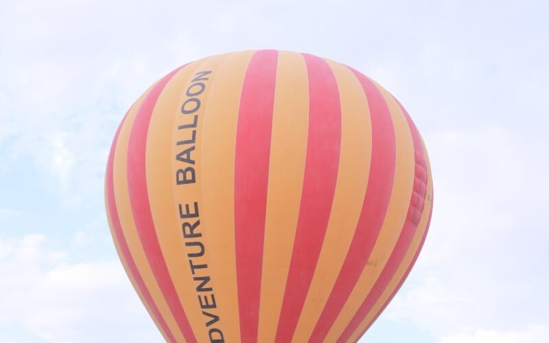 A striped Adventure Balloon envelope rising above the Luxor launch field with other balloons behind