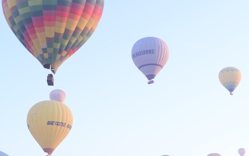 Hot air balloons scattered across a soft pink sunrise sky over Luxor, Egypt