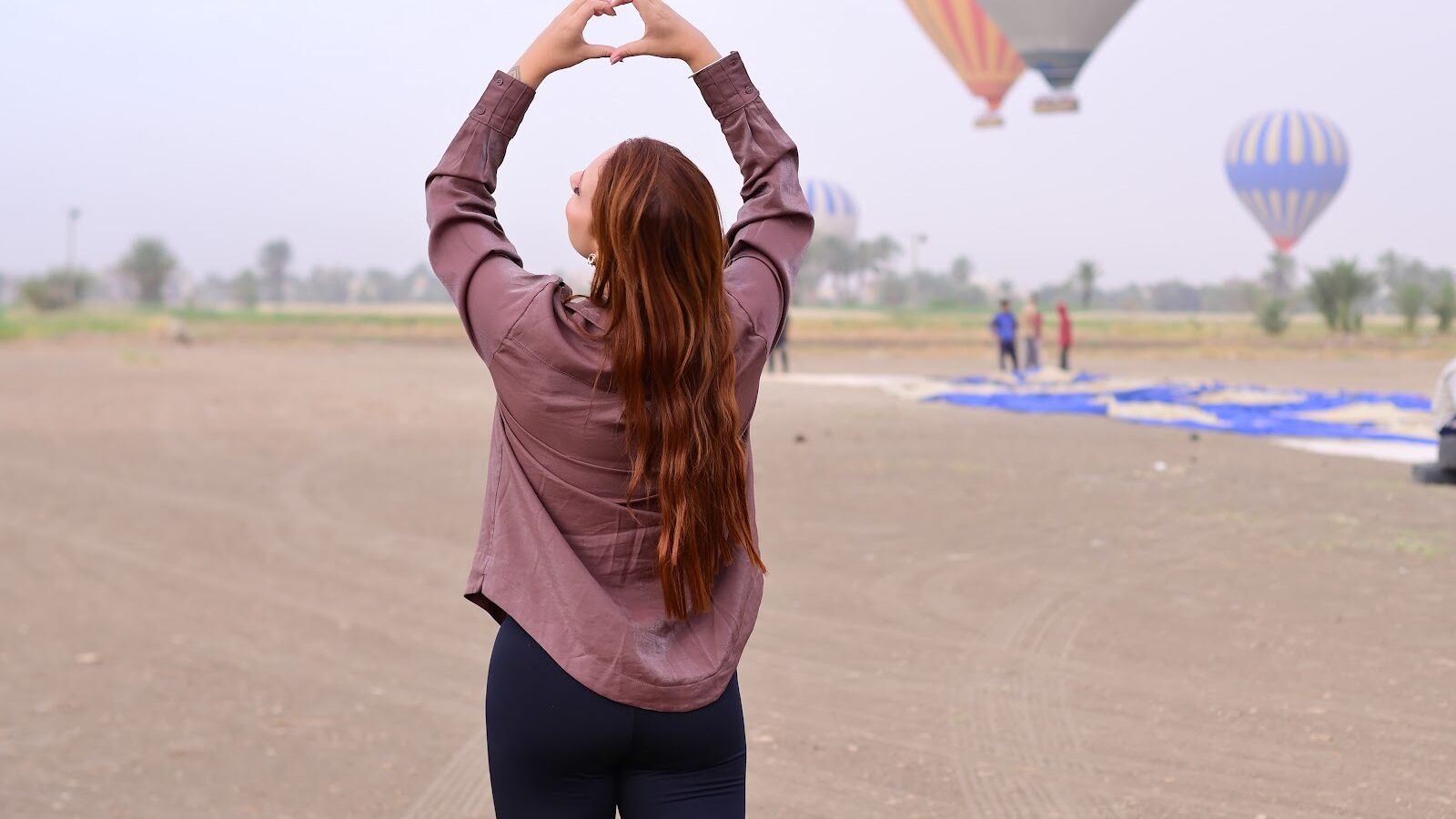 A guest photographed from behind framing a hot air balloon with her hands on the Luxor launch field