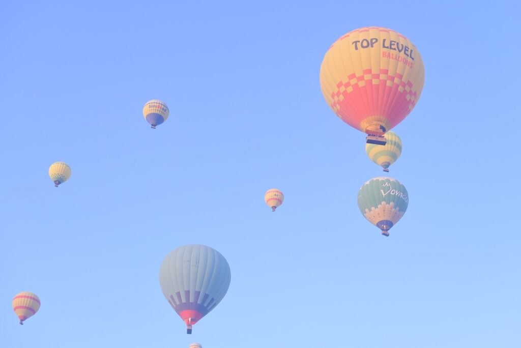 A cluster of hot air balloons drifting across a bright blue sky over Luxor