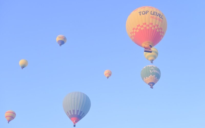 A cluster of hot air balloons drifting across a bright blue sky over Luxor