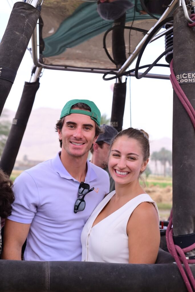 A couple posing in a hot air balloon basket on the Luxor launch field before sunrise