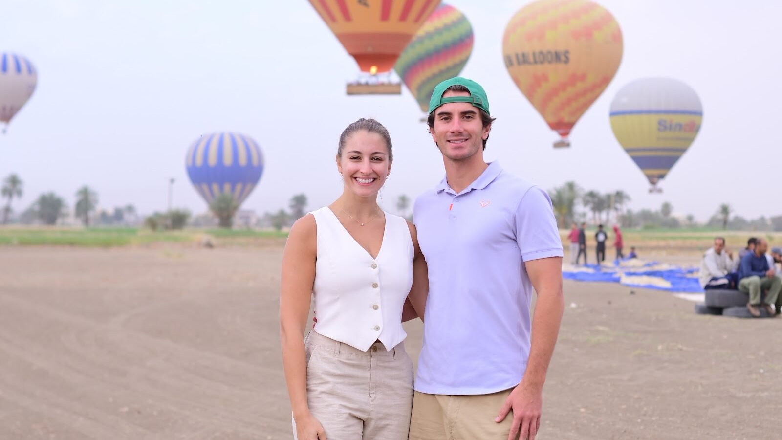 A couple photographed together with hot air balloons rising behind them on the Luxor launch field