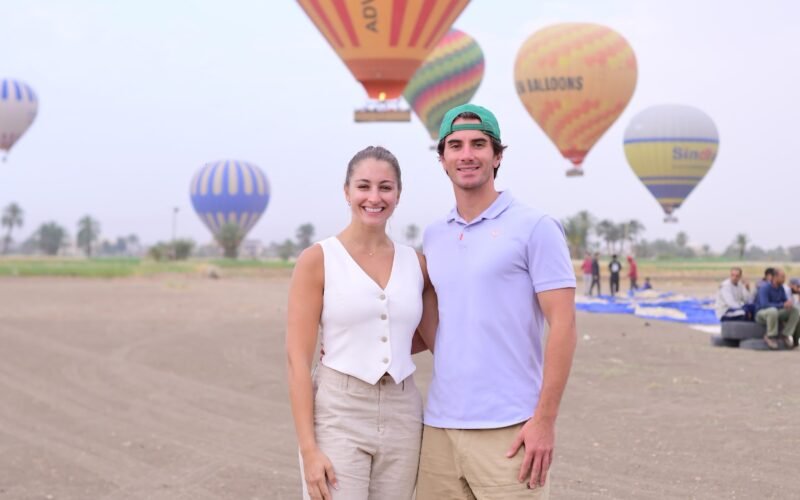 A couple photographed together with hot air balloons rising behind them on the Luxor launch field