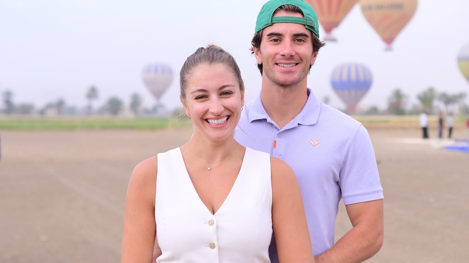 A portrait of a couple standing together with hot air balloons in the sky behind them in Luxor