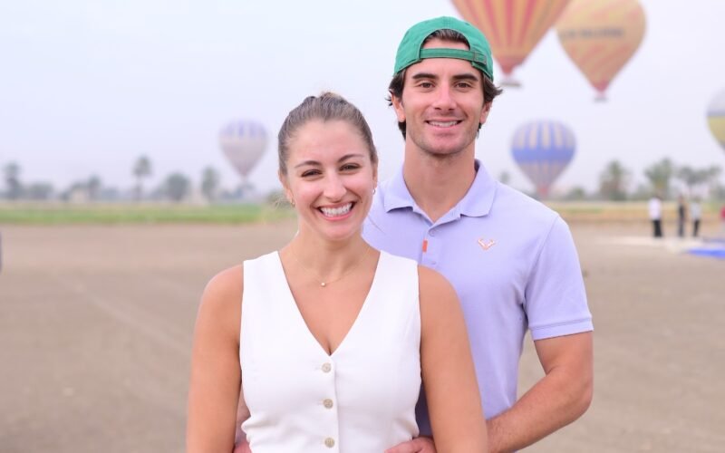 A portrait of a couple standing together with hot air balloons in the sky behind them in Luxor