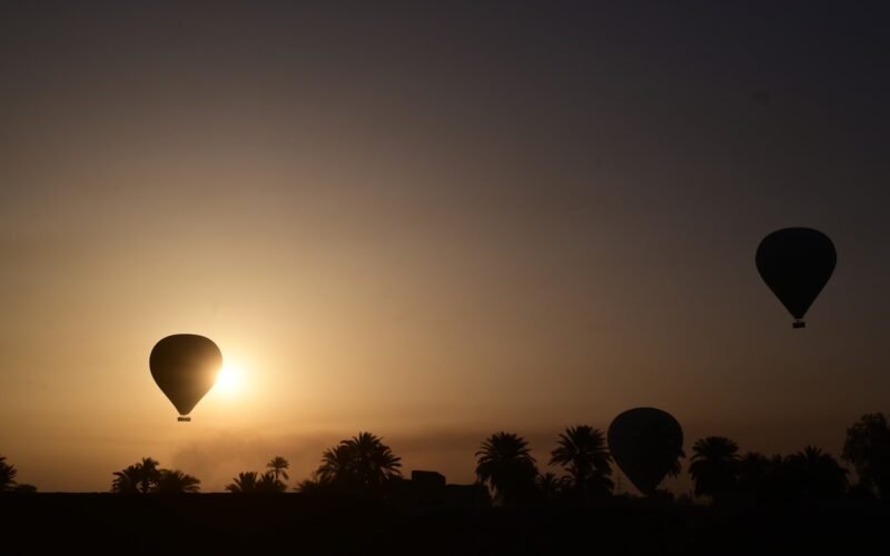 Two hot air balloons silhouetted on the horizon as the sun rises over Luxor