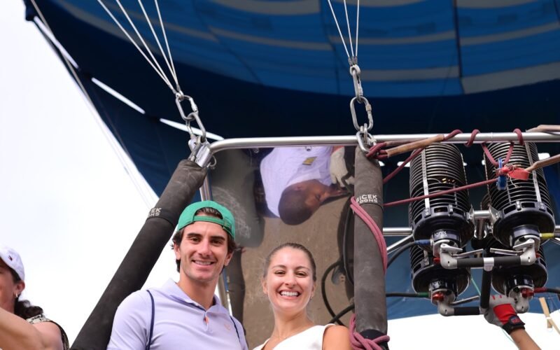 A group of passengers in a hot air balloon basket seen from below with the blue envelope overhead