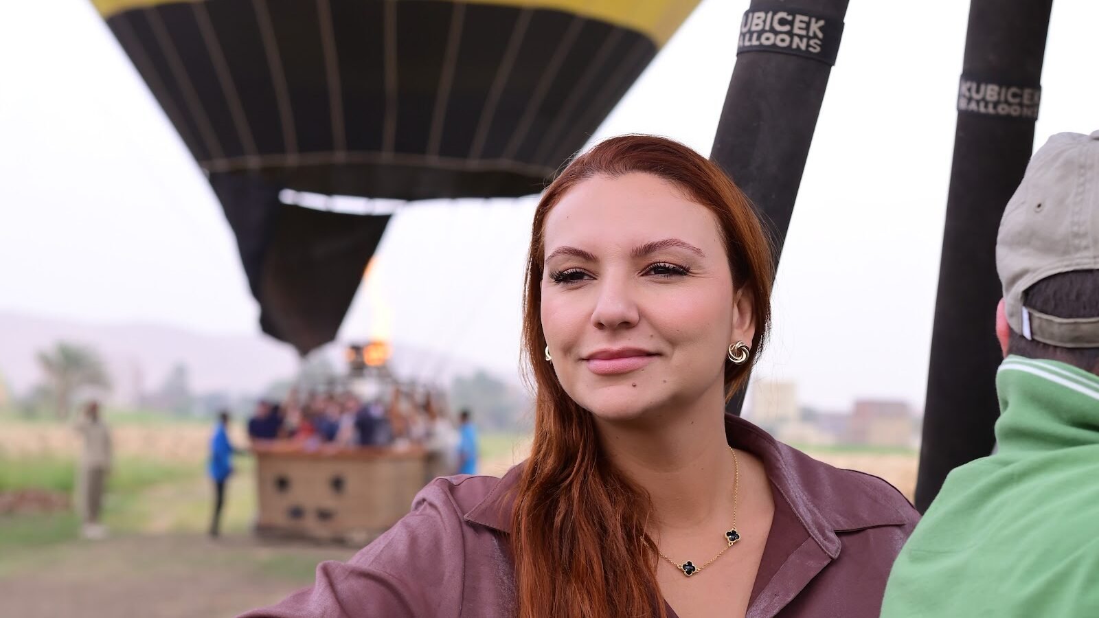 A guest smiling in a hot air balloon basket beneath a bright yellow envelope in Luxor