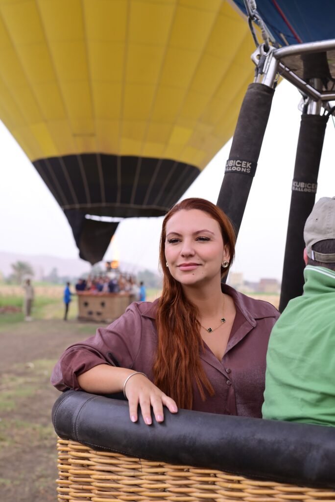 A guest smiling in a hot air balloon basket beneath a bright yellow envelope in Luxor