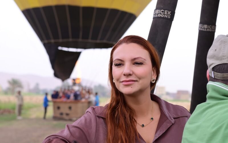A guest smiling in a hot air balloon basket beneath a bright yellow envelope in Luxor