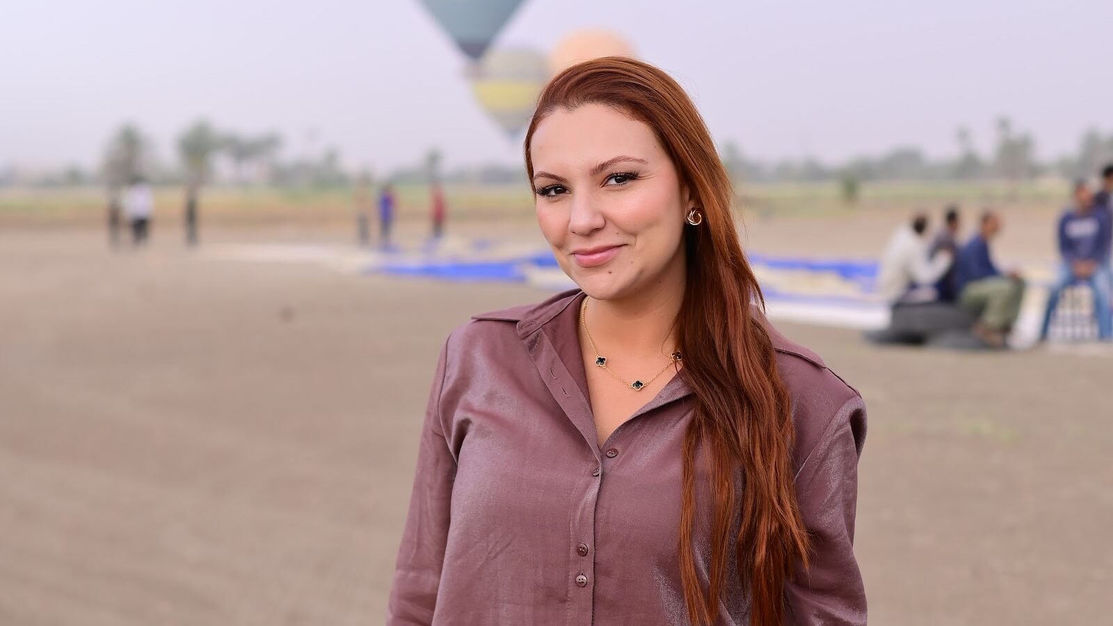 A guest photographed smiling at the Luxor balloon launch field with balloons in the sky behind