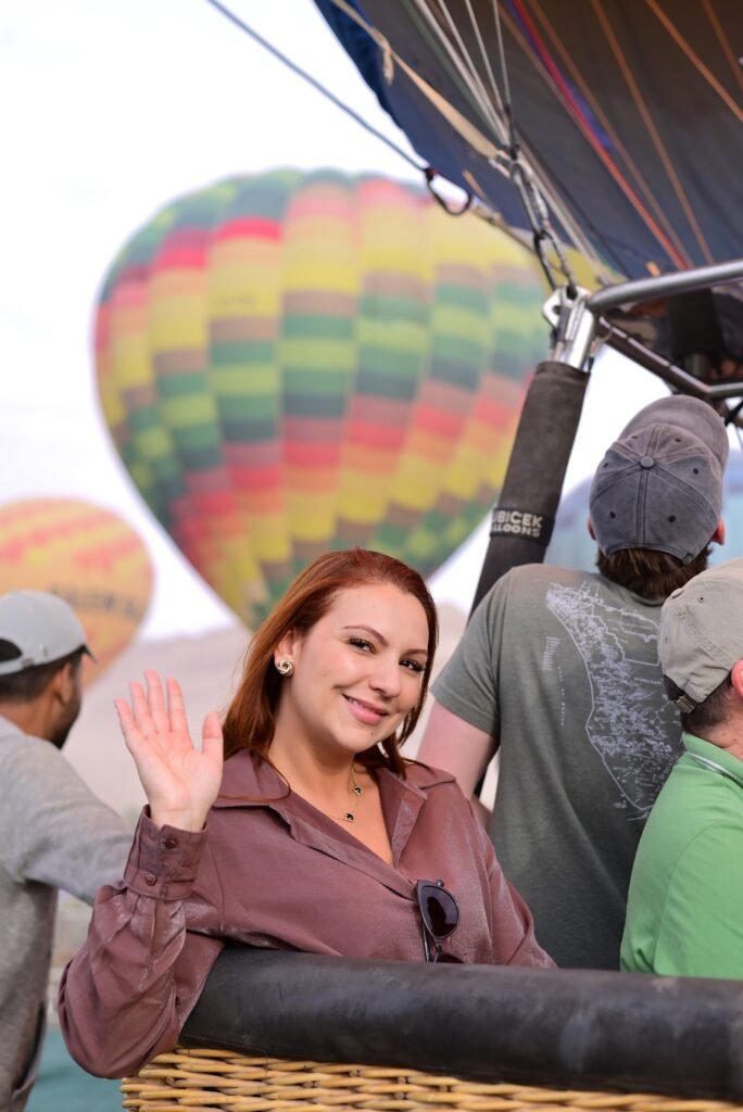 A guest waving from a hot air balloon basket with another balloon flying alongside over Luxor