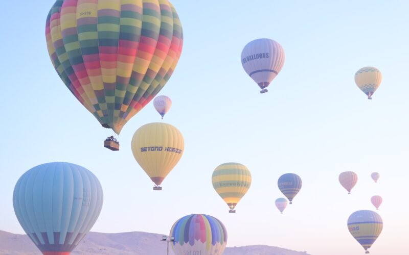 Many colourful hot air balloons climbing together into the pale morning sky above Luxor