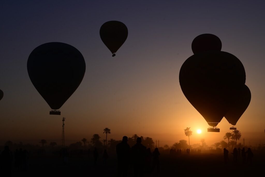 Three hot air balloons silhouetted against a golden sunrise above a line of palm trees in Luxor