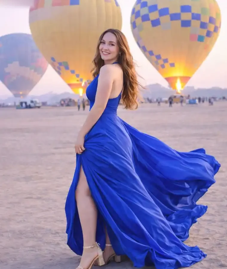 Guest in a blue gown photographed in front of two hot air balloons inflating with burners lit in Luxor