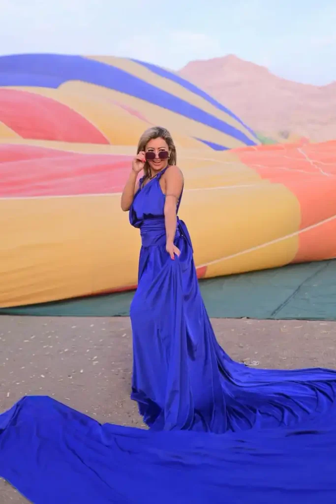 Guest in a blue gown and sunglasses beside a hot air balloon envelope laid out on the Luxor West Bank