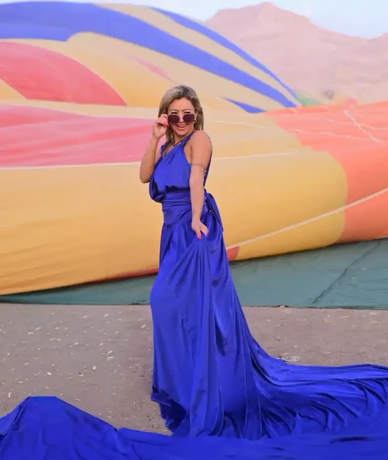 Guest in a blue gown and sunglasses beside a hot air balloon envelope laid out on the Luxor West Bank