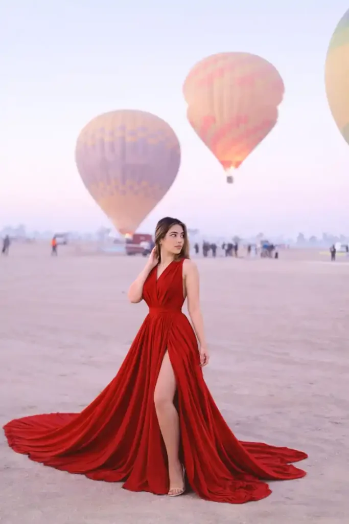Guest in a red gown photographed with hot air balloons airborne over Luxor at sunrise