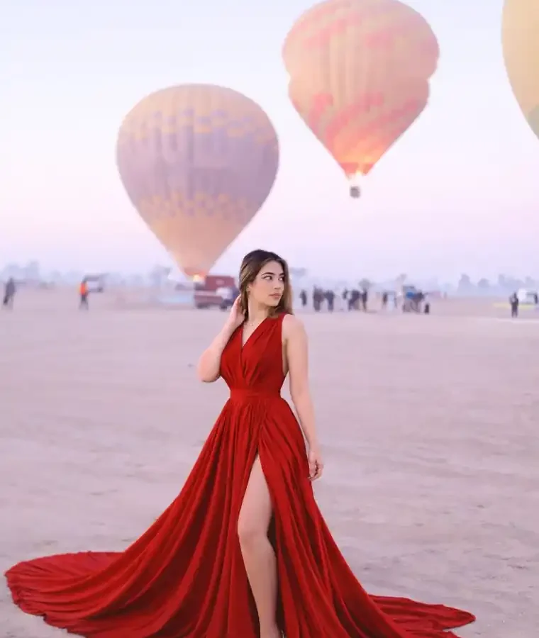 Guest in a red gown photographed with hot air balloons airborne over Luxor at sunrise