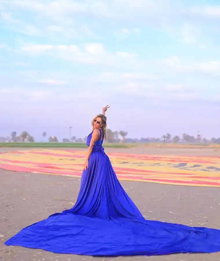 Guest in a blue gown with arm raised beside a hot air balloon envelope on the ground in Luxor