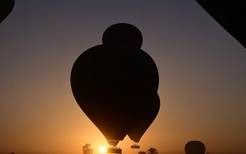 A hot air balloon silhouetted against the rising sun over the Luxor horizon