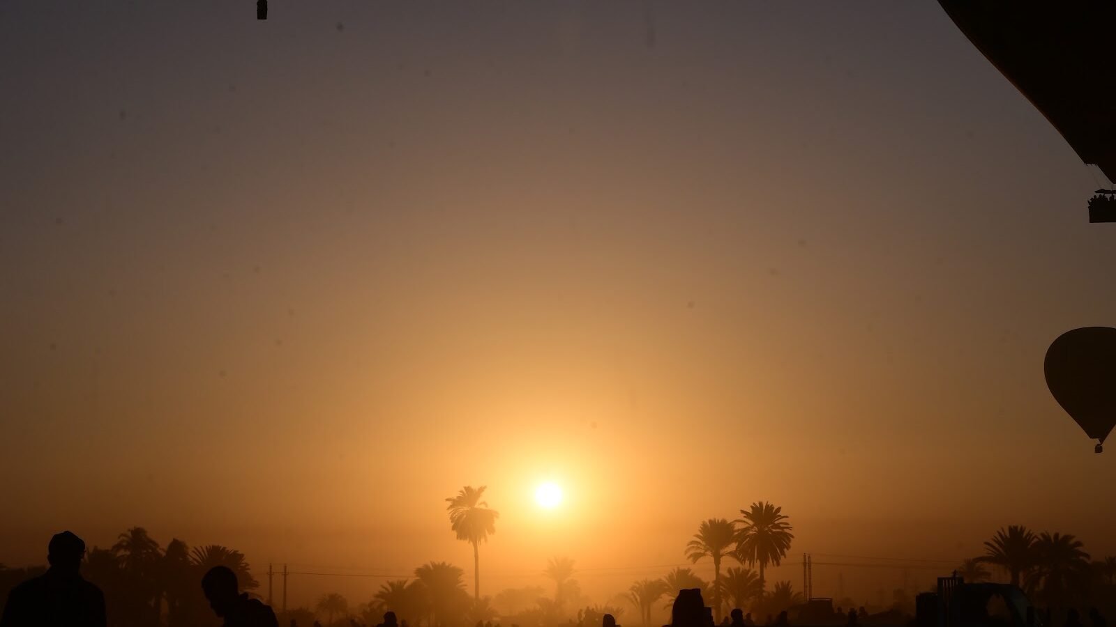 The sun rising through haze over Luxor's West Bank with a balloon silhouetted alongside
