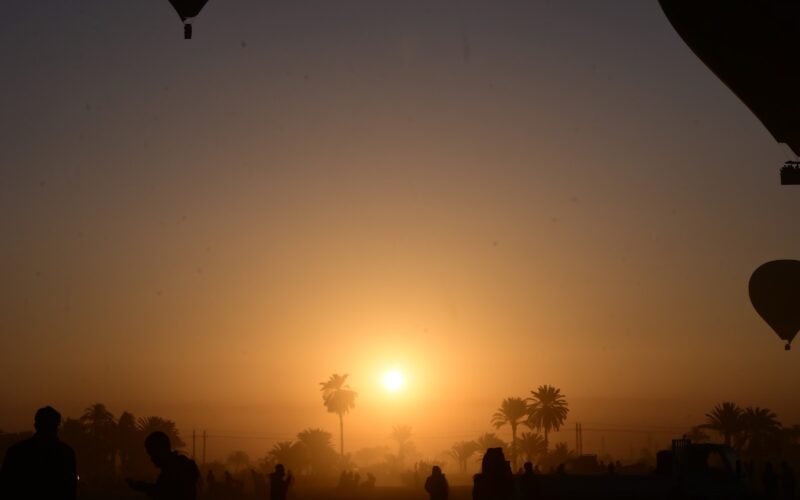 The sun rising through haze over Luxor's West Bank with a balloon silhouetted alongside
